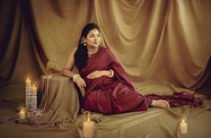 a woman in a red sari sitting on a brown cloth with candles around her