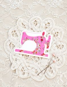 a pink sewing machine pin sitting on top of a lace covered tablecloth with scissors