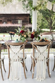 an outdoor dining area with macrami chairs and wooden table topped with fruit, flowers and greenery