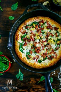 a pizza with bacon, spinach and cheese in a skillet on a wooden table