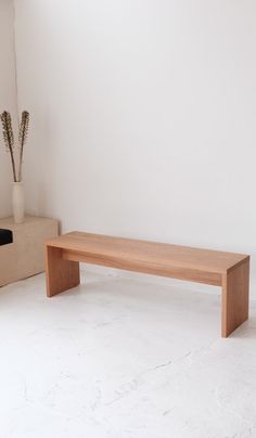 a wooden bench sitting on top of a white floor next to a vase filled with flowers