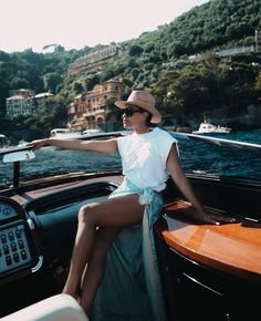 a woman sitting on the back of a boat with her legs crossed and wearing a hat