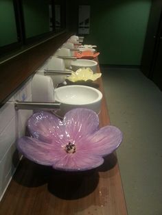 a row of sinks in a public restroom with flowers on the counter top and bowls