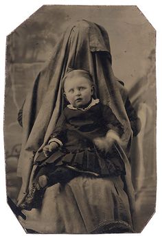 an old black and white photo of a baby wearing a dress with a veil on it's head