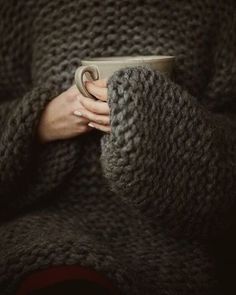 a woman is holding a coffee cup in her hands while wearing a knitted sweater