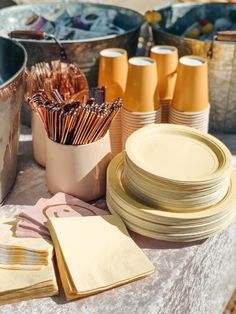 a table topped with plates and cups filled with gold colored napkins next to other dishes