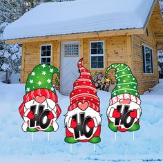 three christmas gnomes standing in front of a cabin