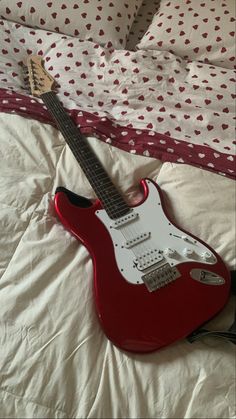 a red guitar laying on top of a bed