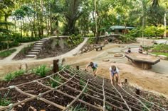 children playing in an outdoor play area at a park with trees and rocks on the ground