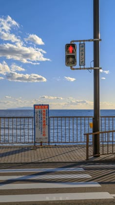 a traffic light sitting on the side of a road next to the ocean under a cloudy blue sky