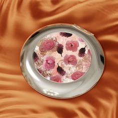 a silver plate with pink flowers in it on a brown satin table cloth, top view