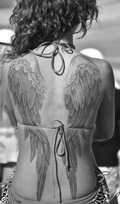 the back of a woman's body with tattoos on her chest and wings above it