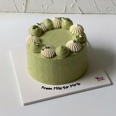 a green cake with white frosting and sea shells on top is sitting on a card