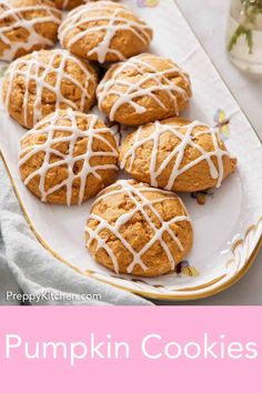 pumpkin cookies with white icing on a pink and white plate next to a jar of flowers