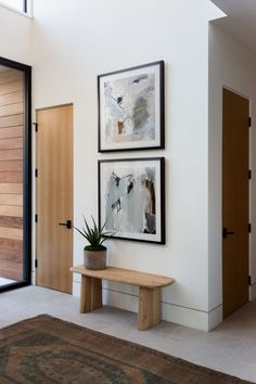 two framed pictures hang on the wall above a wooden bench in front of a door