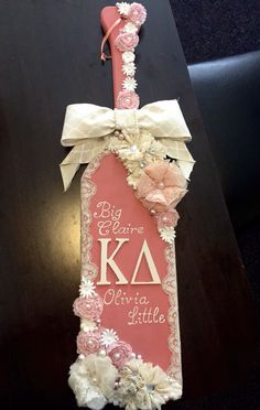 a pink and white sign with flowers hanging from it's side on a table