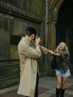 a man taking a picture of a woman in front of an old building with a camera