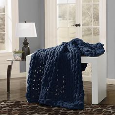 a blue blanket is sitting on a white bench in front of a window and lamp