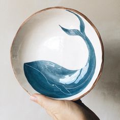 a hand holding a bowl with a blue whale painted on it