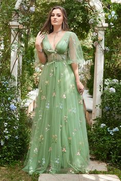 a woman wearing a green dress standing in front of a gazebo with flowers on it