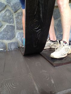 a man standing on top of a wooden platform next to a black skateboard in front of a stone wall