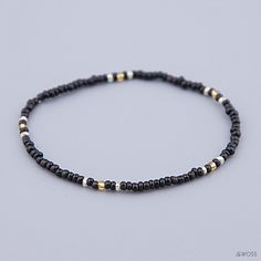 a beaded bracelet with black beads and gold accents on a gray background, showing the clasp