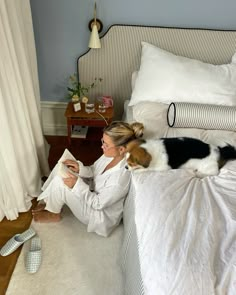 a woman sitting on the floor reading a book with her dog laying next to her