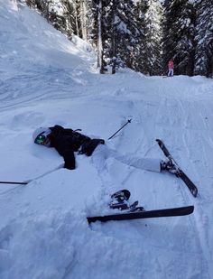 two skis laying in the snow with one person standing next to them and another lying down