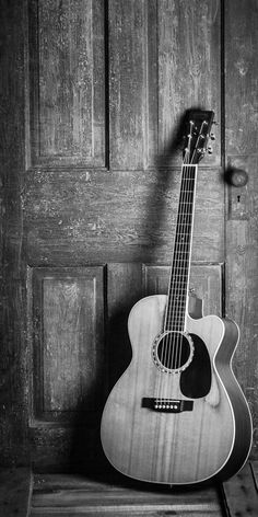 black and white photograph of an acoustic guitar leaning against a wooden door with its shadow on the floor