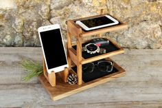 a cell phone and some other items in a wooden holder on a table next to a stone wall