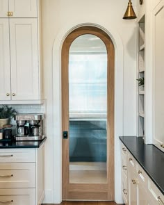 a kitchen with white cabinets and black counter tops next to a wooden door that leads to an arched window