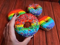 a hand holding a doughnut with rainbow sprinkles on it and another donut in the background