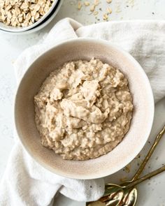 a bowl filled with oatmeal sitting on top of a white table next to spoons