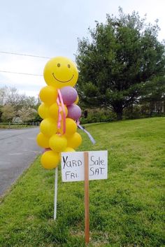 a yard sale sign with balloons in the shape of a smiley face