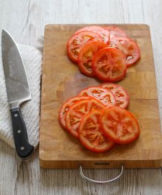 sliced tomatoes sit on a cutting board next to a knife