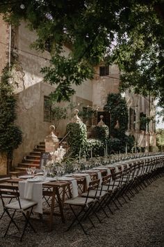 a long table set up with white linens and place settings in front of an old building