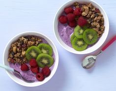 two bowls filled with fruit and granola on top of a white table