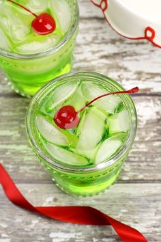 two glasses filled with ice and cherries next to a red ribbon on a wooden table