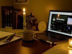 an open laptop computer sitting on top of a wooden desk next to a lit candle