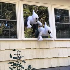 two stuffed animals are in the window of a house, one is white and the other is black