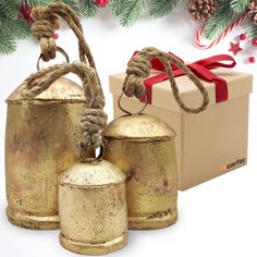 three gold bell ornaments are next to a box with a red ribbon and christmas decorations