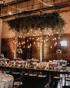 the tables are set up with white linens and greenery hanging from the ceiling