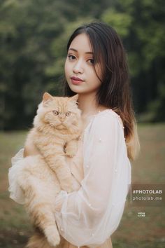 a woman holding a cat in her arms and posing for the camera with trees in the background