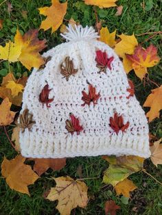 a crocheted hat with leaves on it laying in the grass next to autumn leaves