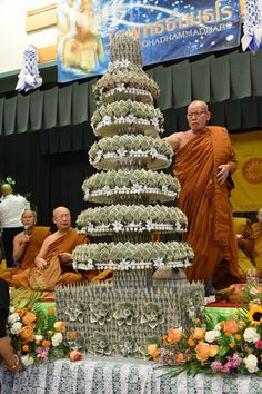 there is a man standing next to a cake made out of stacks of money in front of other people