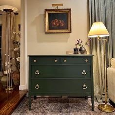 a green dresser in a living room next to a lamp and painting on the wall