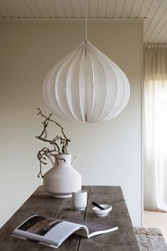 a table with a book and vase on it next to a lamp hanging from the ceiling