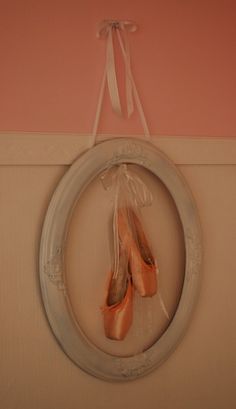 two pairs of ballet shoes hanging on a wall in front of a round frame with ribbon