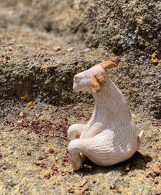 a small ceramic animal sitting on the ground next to a rock wall and dirt area