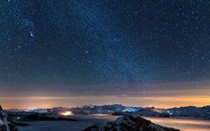 the night sky is filled with stars above some snow covered mountains and water below it